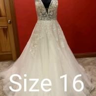 White, lace-embellished A-line wedding dress with a deep V-neckline, displayed on a mannequin, labeled size 16.