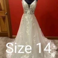 An off-white, floor-length A-line wedding dress with floral lace detailing, a V-neckline, and a size 14 label overlaid.