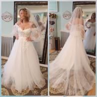 A person wearing a white off-the-shoulder wedding gown with puffed sleeves and a veil, shown from the front and back.