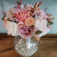 A bouquet of silk roses in shades of pink, peach, and white, resting in a glass vase filled with white pearl beads.