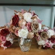 A central bouquet of burgundy, dusty rose, and white silk roses with gold accents displayed in a glass vase.