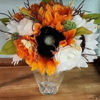 A bouquet of orange and white flowers, including a prominent black-centered sunflower, in a clear glass vase.