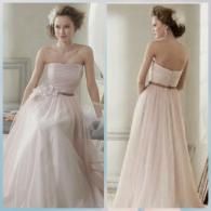 A woman wearing a pale pink, strapless, A-line gown with a floral accent at the waist, shown from the front and back.