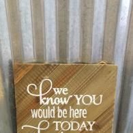 A wooden sign against a corrugated metal wall, inscribed with: 