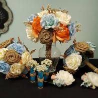 A collection of bouquets, boutonnieres, and small vases featuring orange, cream, and light blue artificial flowers.