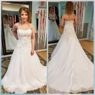 A person wears a strapless white wedding dress with beadwork, shown from the front and back in a clothing store mirror.