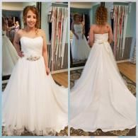 A woman in a strapless white bridal gown with a jeweled waist accessory, shown from the front and back in a boutique.