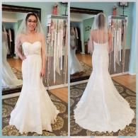 A person in a white strapless wedding gown with a veil, shown from the front and back in a clothing store mirror.