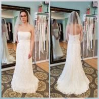 A bride wears a floor-length, strapless white lace gown and a veil, shown from the front and back in a bridal shop mirror.