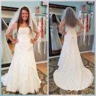 A bride standing in a shop, wearing a white strapless gown and a veil, shown from both the front and the back in a mirror.