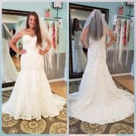 A woman wearing a white, strapless, lace mermaid-style wedding dress and veil, shown from the front and back in a mirror.