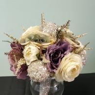 A bridal bouquet of cream and mauve roses mixed with gold-dusted foliage and sparkling, jeweled spheres.