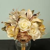 A wedding bouquet of cream and beige artificial roses with decorative pearls and feathers in a clear glass vase.