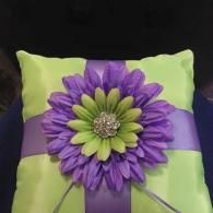 A lime green ring bearer pillow with a purple satin ribbon and a large purple and green daisy with a rhinestone center.