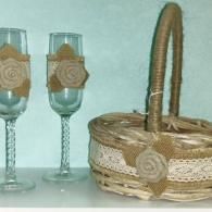 Two champagne flutes and a woven basket decorated with matching burlap roses and lace ribbons on a light blue background.