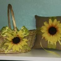 A rustic woven basket and a small, burlap ring bearer pillow, both decorated with green ribbon and a large sunflower.