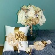 A white and gold ring bearer pillow, matching floral bouquet in a glass vase, a boutonniere, and a floral garter.