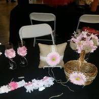 Wedding accessories including a ring pillow, flower basket, champagne flutes, and a garter on a black tablecloth.