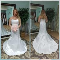 A person stands in a bridal shop wearing a strapless white wedding dress with a train, shown from the front and back.