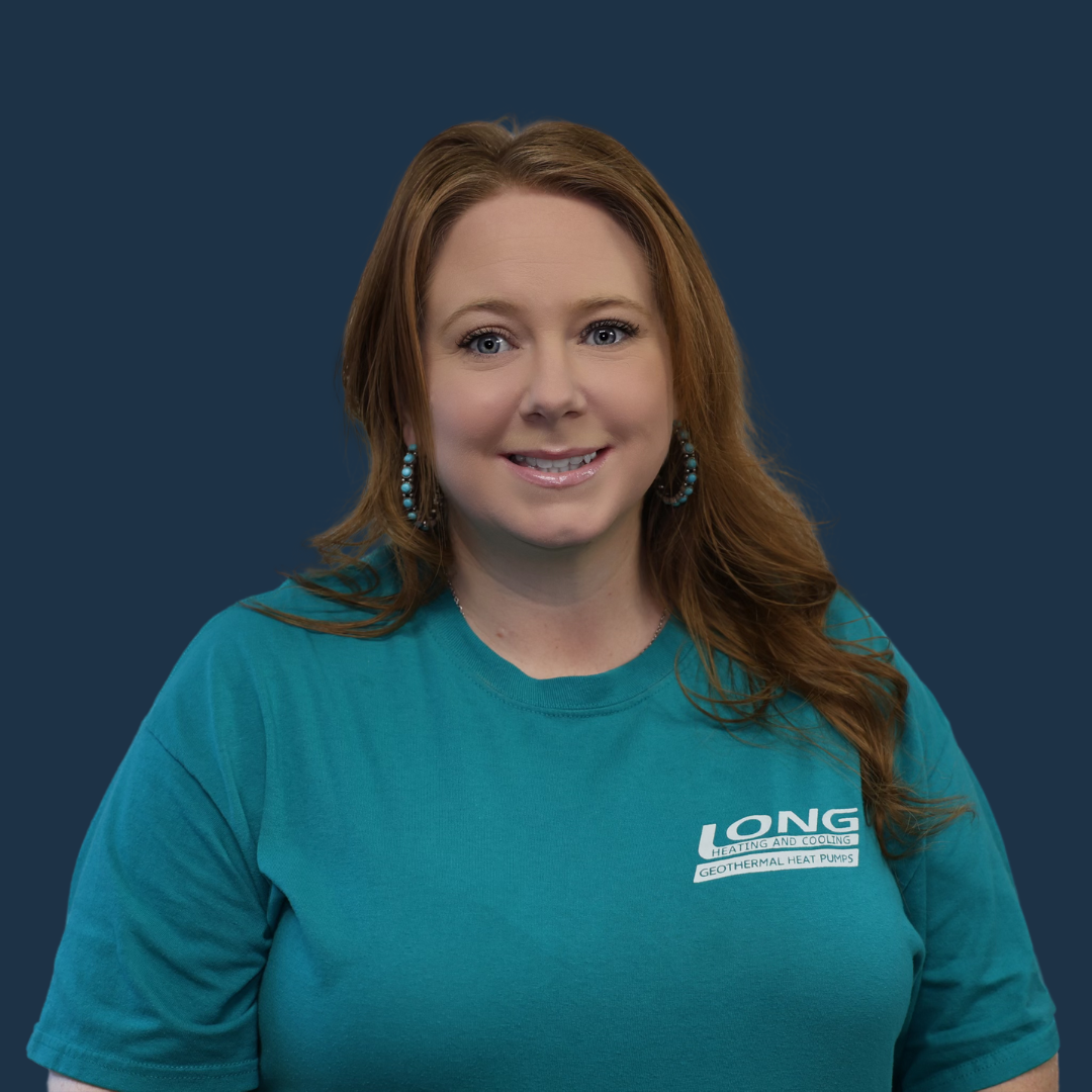 Woman with auburn hair, wearing a turquoise shirt with a logo, smiles at the camera.