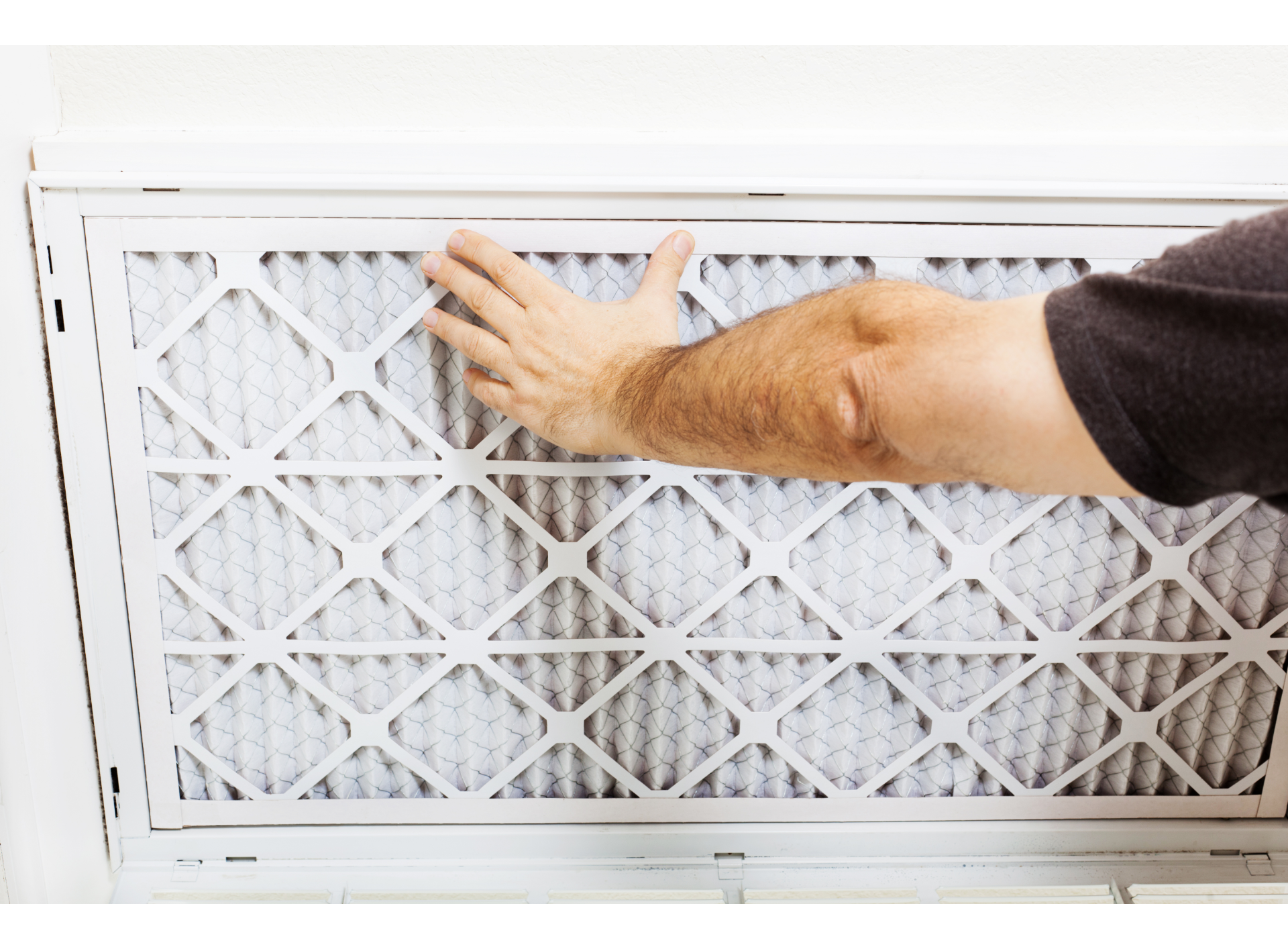 Person's hand removing an air filter from a white vent. Filter is covered in grey.