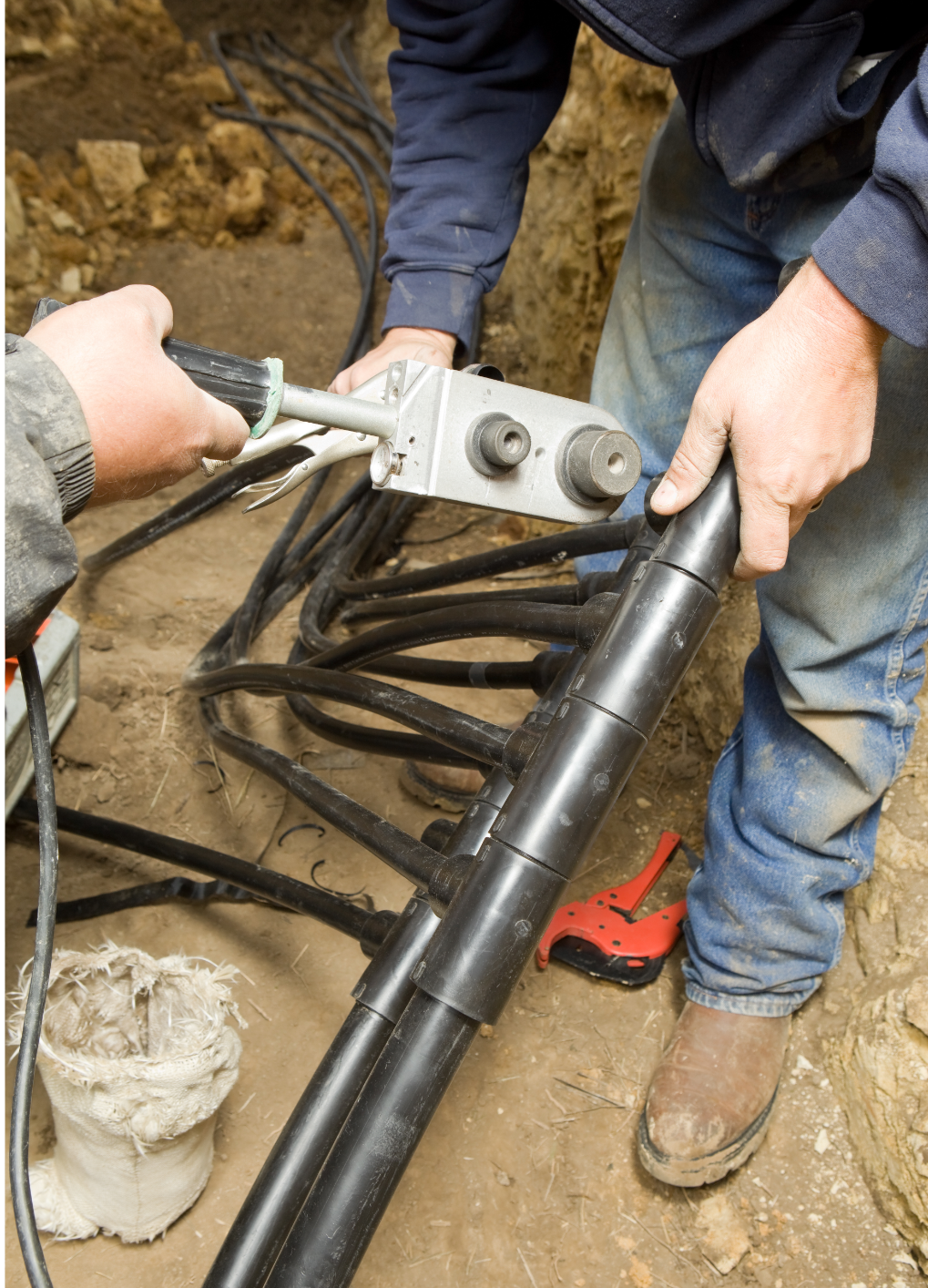 Two workers using a fusion tool to join black pipes in a trench.