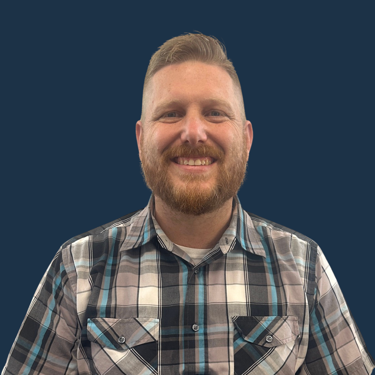 Elderly man in plaid shirt smiles at camera, set against a blue background.