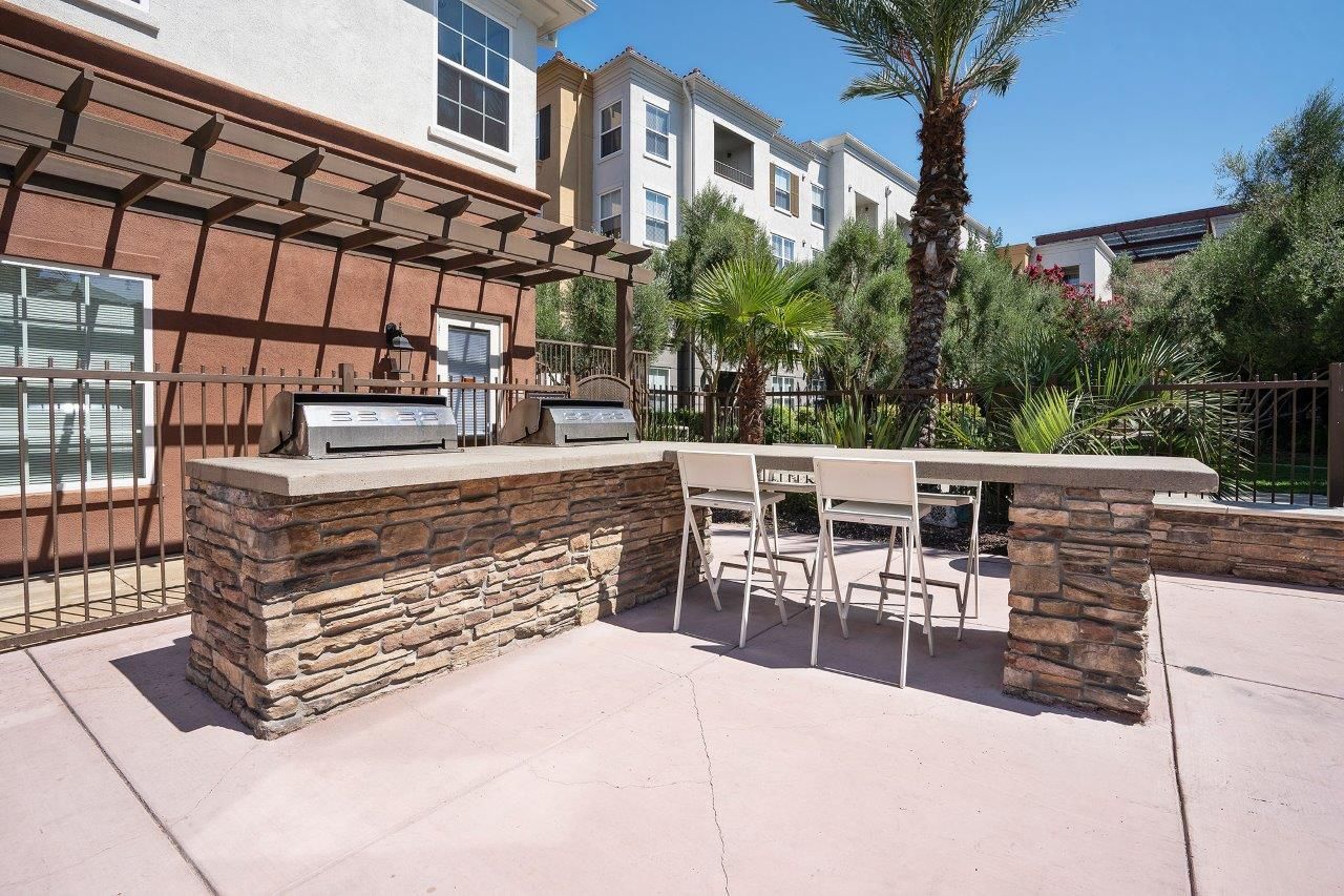 Outdoor community barbecue area with stone counter, built-in grills, and four white stools.
