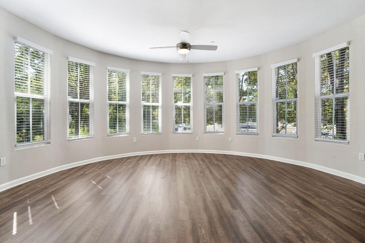 Bright empty living room with a curved wall of windows, wood-look flooring, and a ceiling fan.