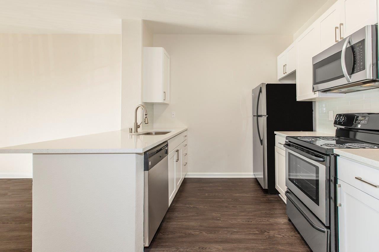 Modern kitchen with white cabinets, stainless steel appliances, and dark wood flooring.