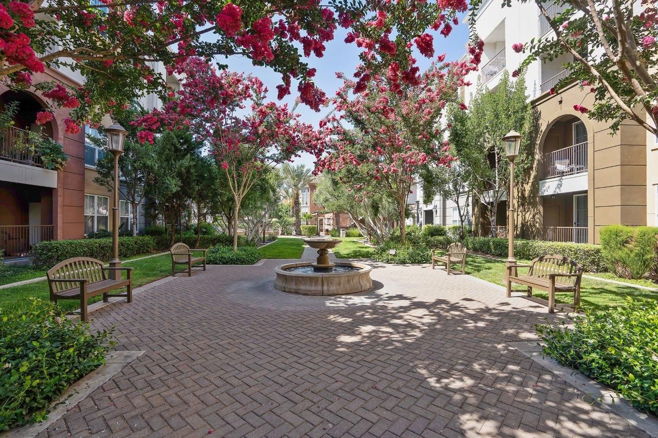 Brick-paved courtyard with a central fountain, benches, and flowering trees between apartment buildings.