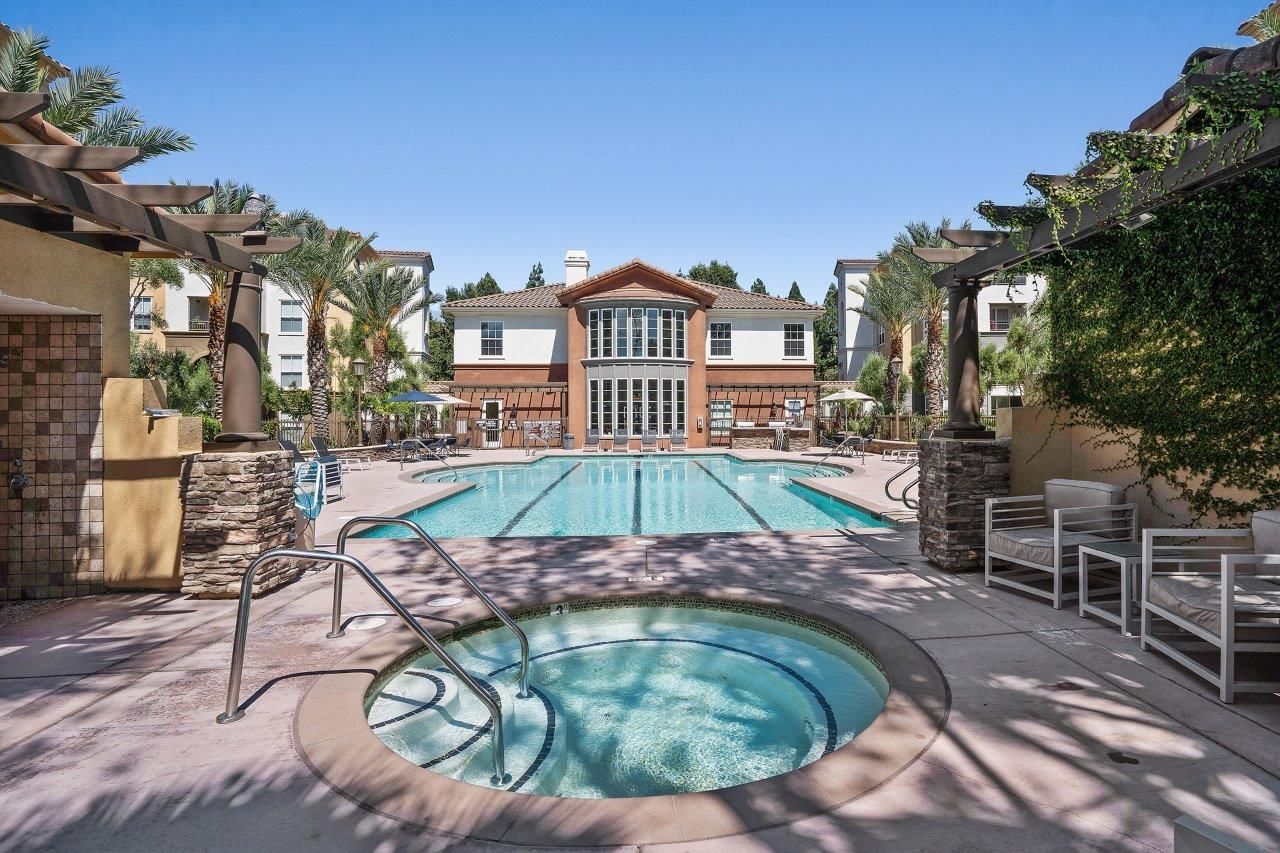 Outdoor communal pool area with a rectangular pool, circular hot tub, lounge chairs, and palm trees.