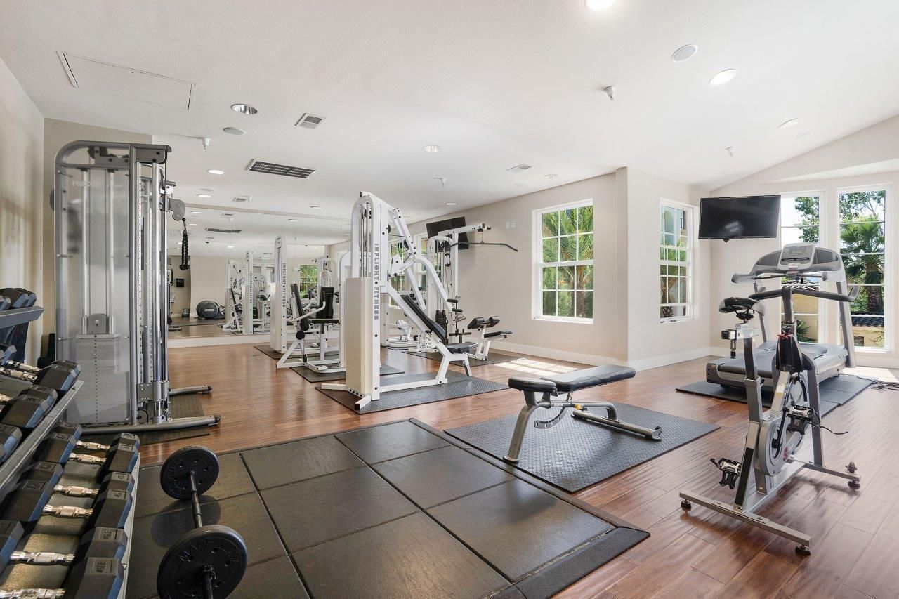 Bright communal fitness center with cardio machines, weight machines, free weights, and exercise mats.
