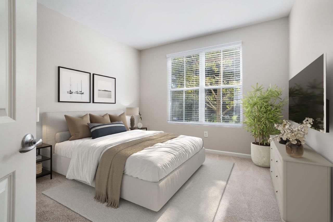 Modern bedroom with a king bed, dresser, TV, and large window.