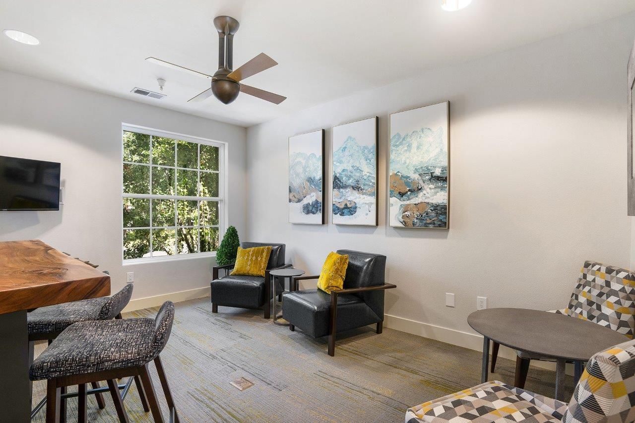 Communal lounge with black armchairs, round tables, and a large window.