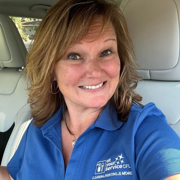 A woman in a blue shirt is smiling while sitting in a car.