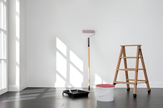 An empty room with a ladder , paint roller , and bucket of paint.