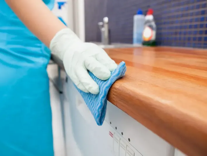 A person is cleaning a kitchen counter with a blue cloth.