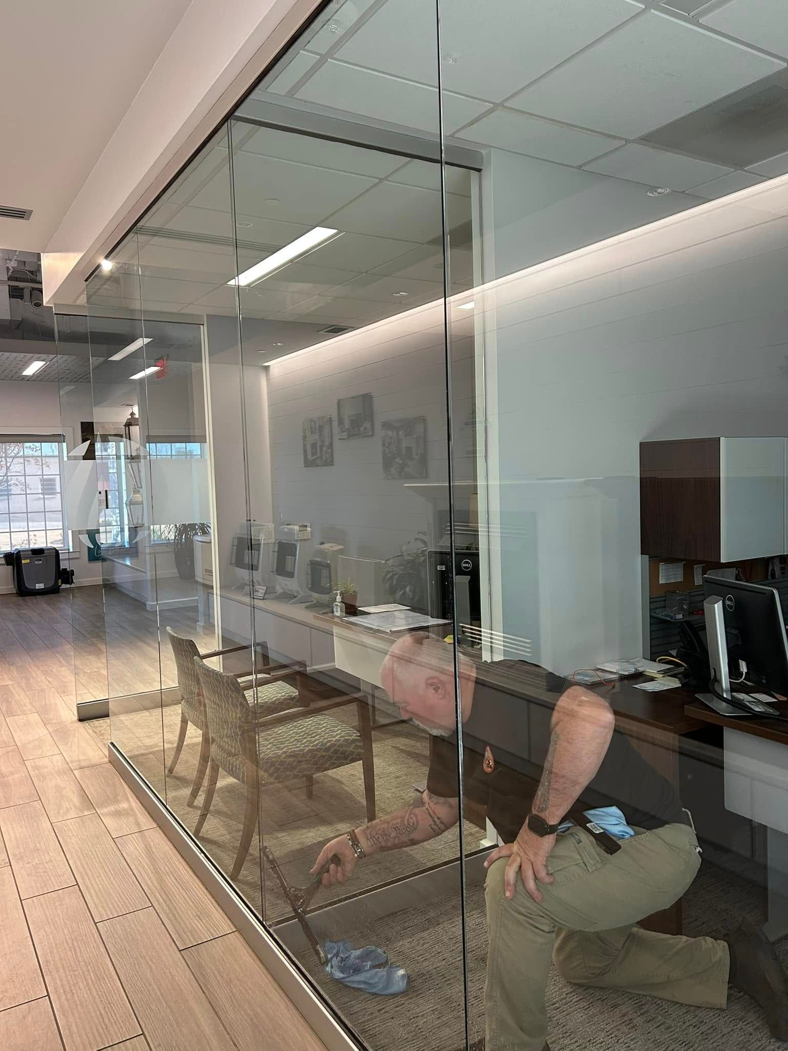A man is kneeling in front of a glass wall in an office.