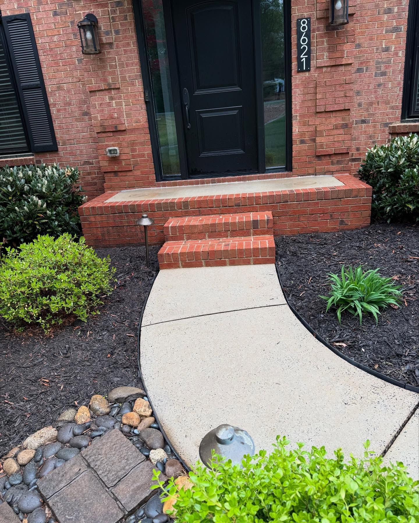 A brick house with a concrete walkway leading to the front door.