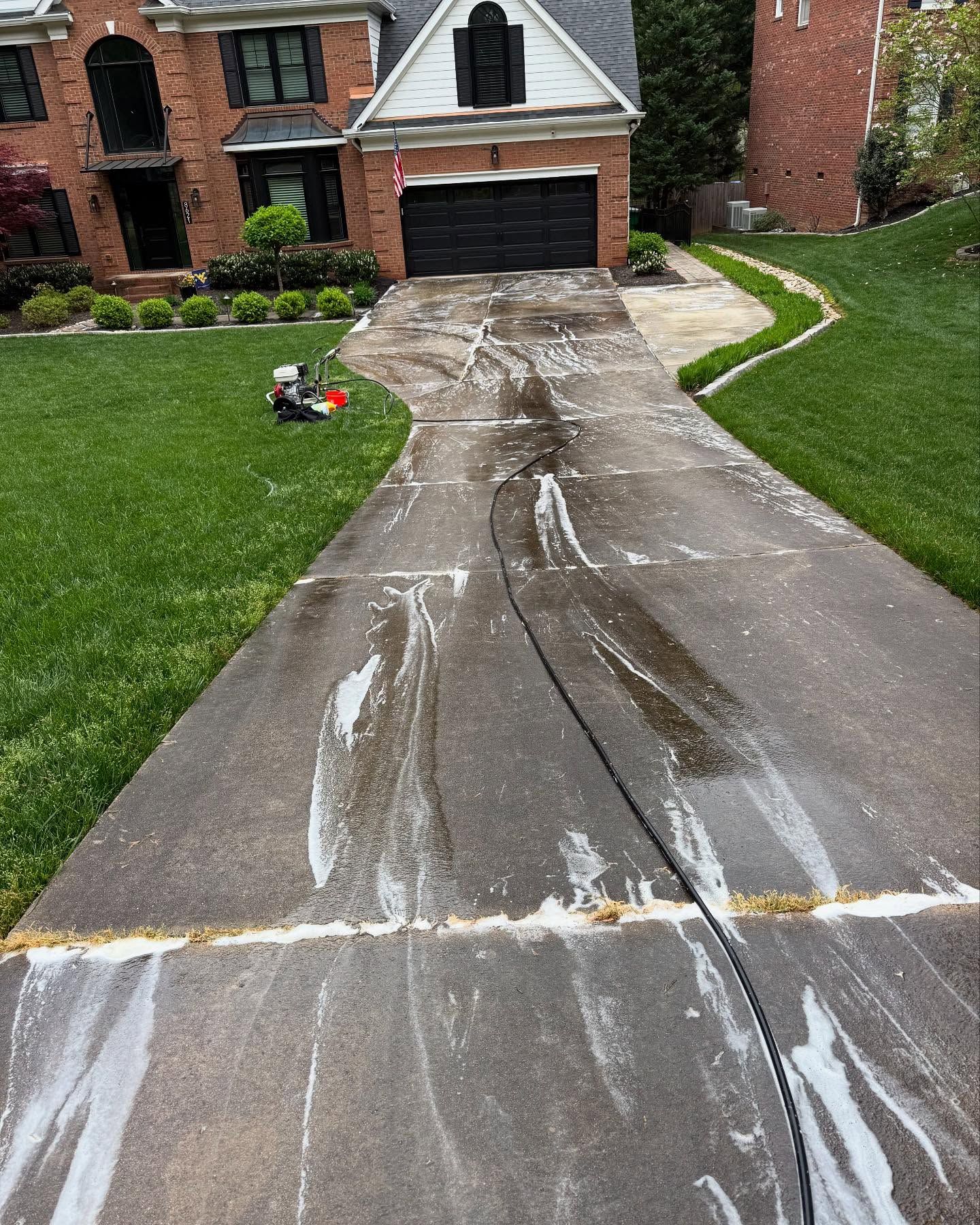 A concrete driveway is being cleaned in front of a brick house.