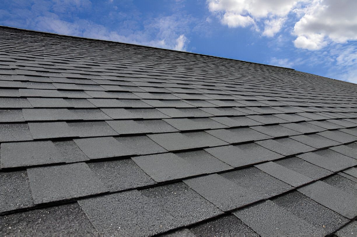Gray asphalt shingle roof against a blue sky with scattered clouds.