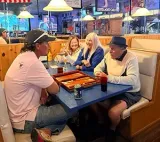 Four people sit at a table in a restaurant playing backgammon.