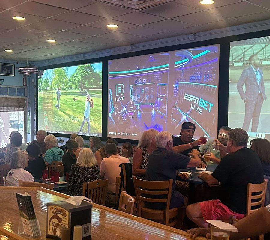 Patrons sit at tables and a bar in a sports bar, watching golf and an ESPN Bet show on large screens mounted on the wall.