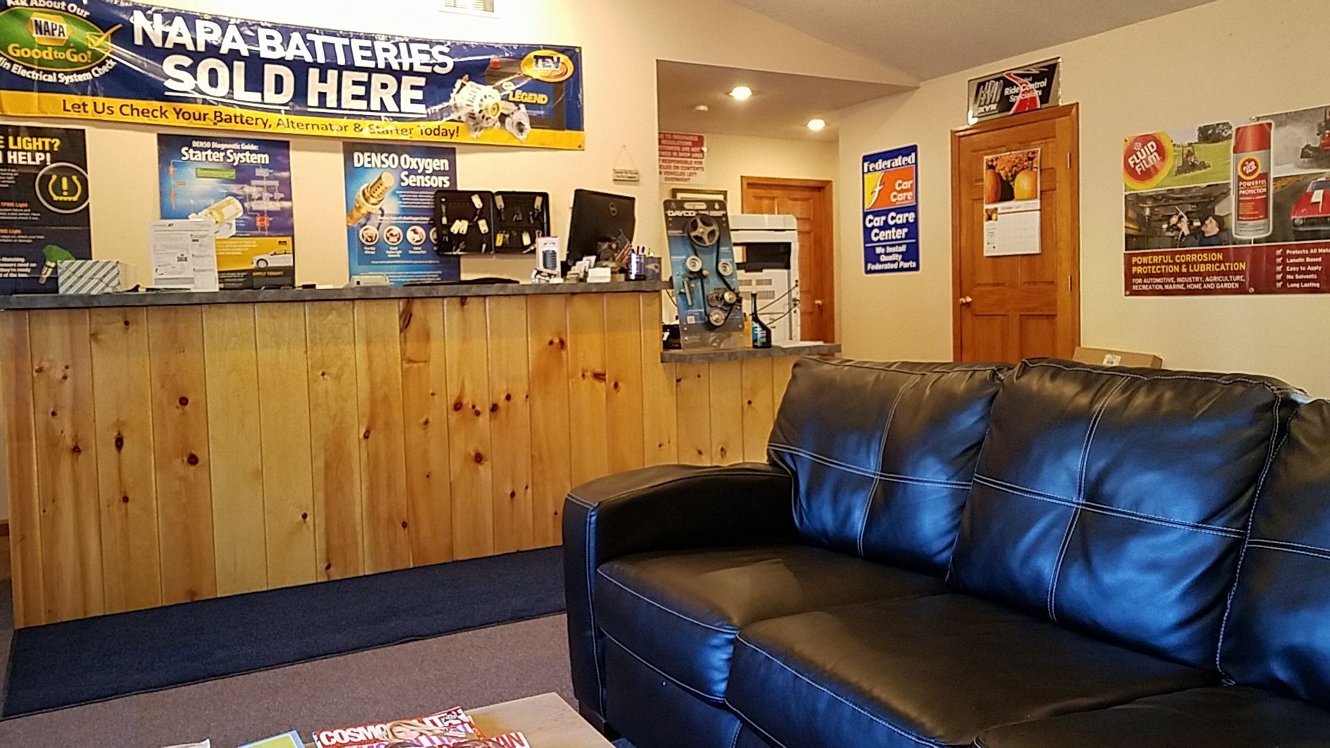 Auto repair shop waiting area with a reception desk, black leather couch, and posters. | Greg's Auto Repair