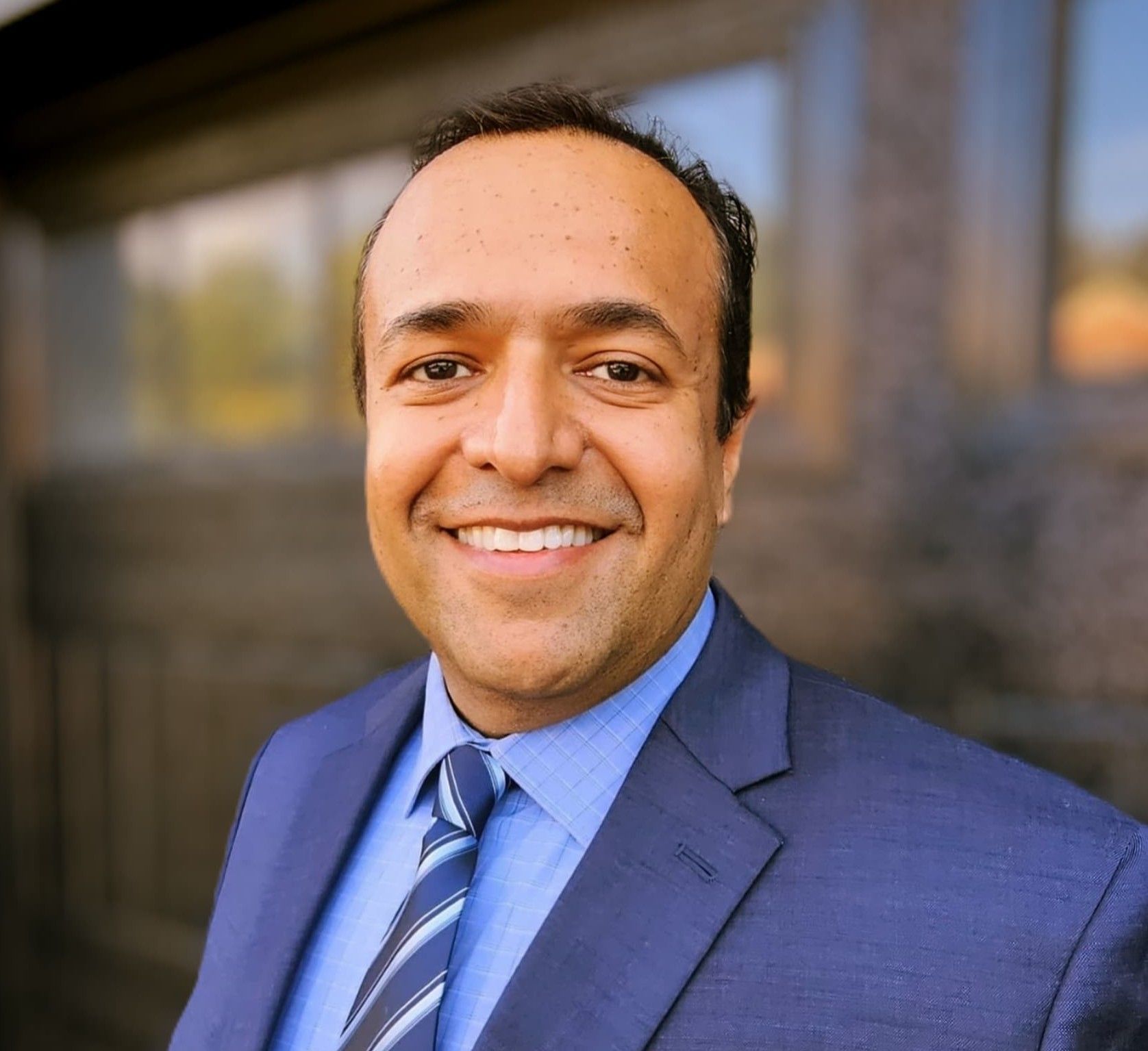 Ali Ikram our founder, standing in front of a building with glass windows.