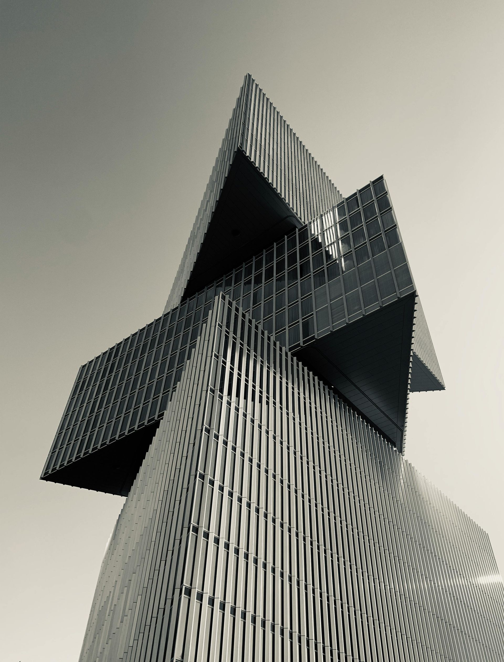 Modern skyscraper with angular, stacked sections against a clear sky. Black and white.