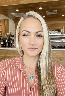 Portrait of a blonde person in a striped shirt, seated in a wood-paneled café, looking at the camera
