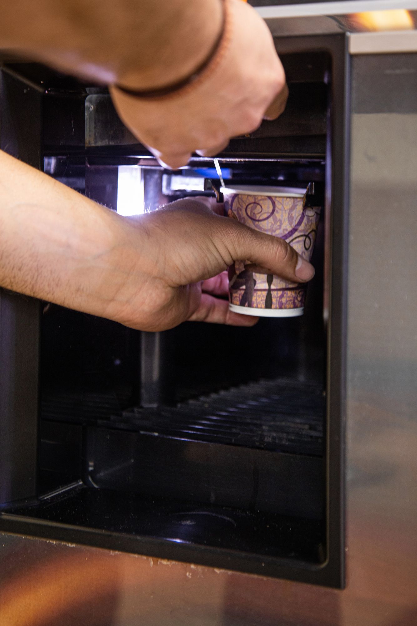 Persona che riempie un bicchiere di carta con il liquido di un distributore di bevande.