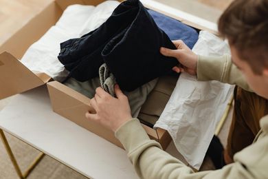 A man is opening a cardboard box filled with clothes.